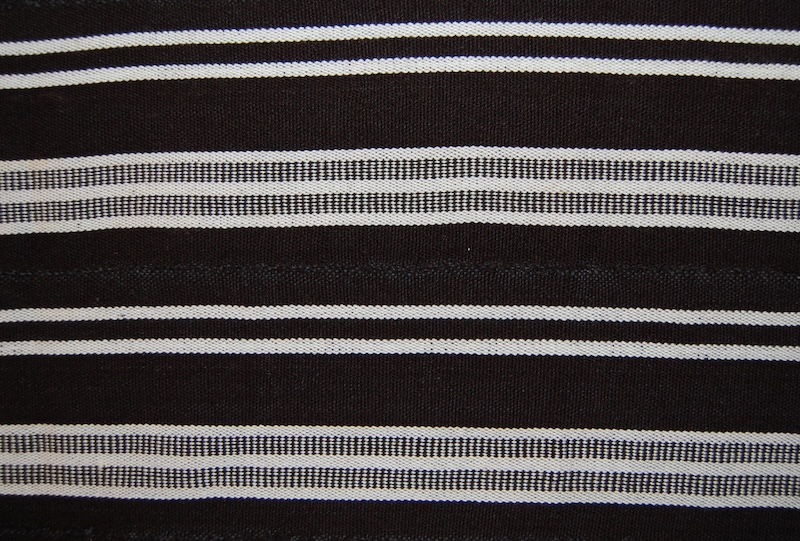 Warp-faced wrapper made of cotton. Twelve narrow strips hand-sewn together. Black and white cotton warp and black cotton weft. Loose warp thread fringes at each end.